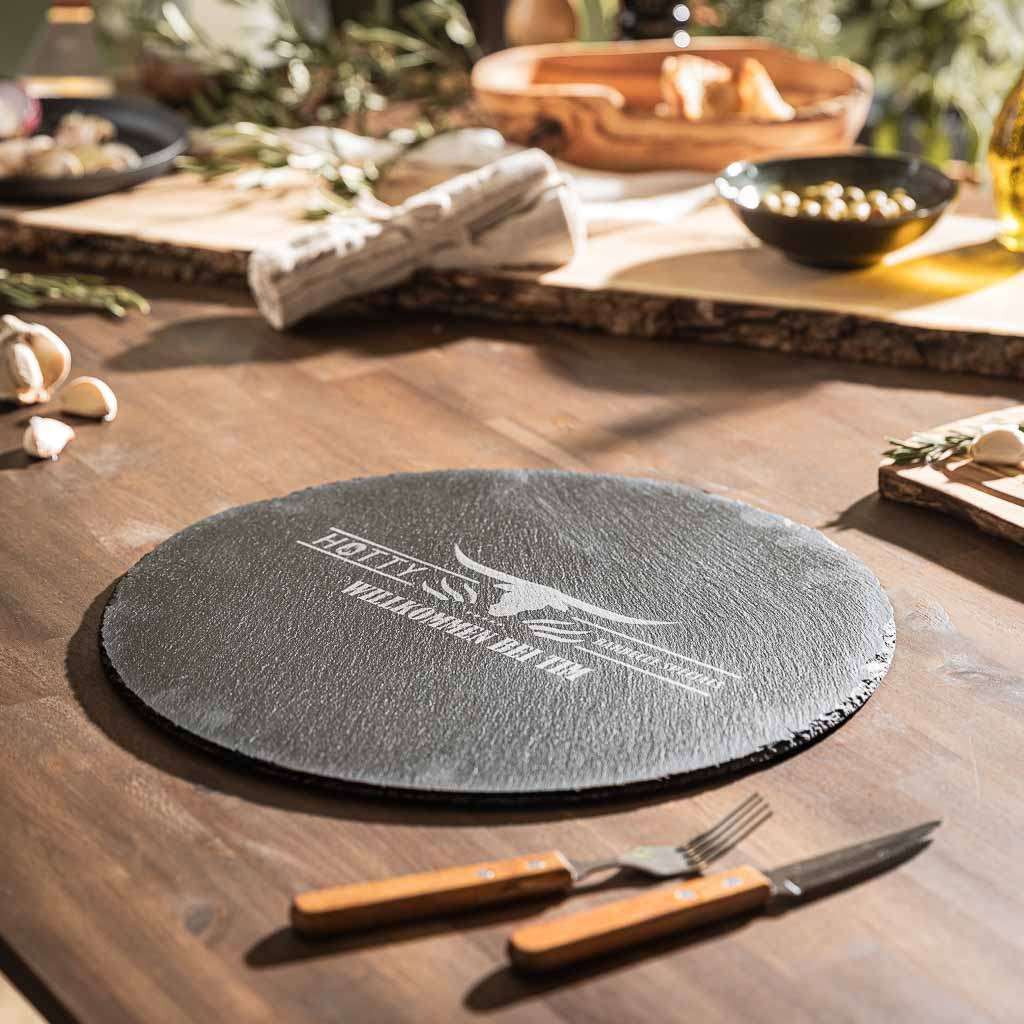 Schiefer-Tischset auf Holztisch mit rustikaler Optik, rundes Design mit Personalisierungsmöglichkeit.