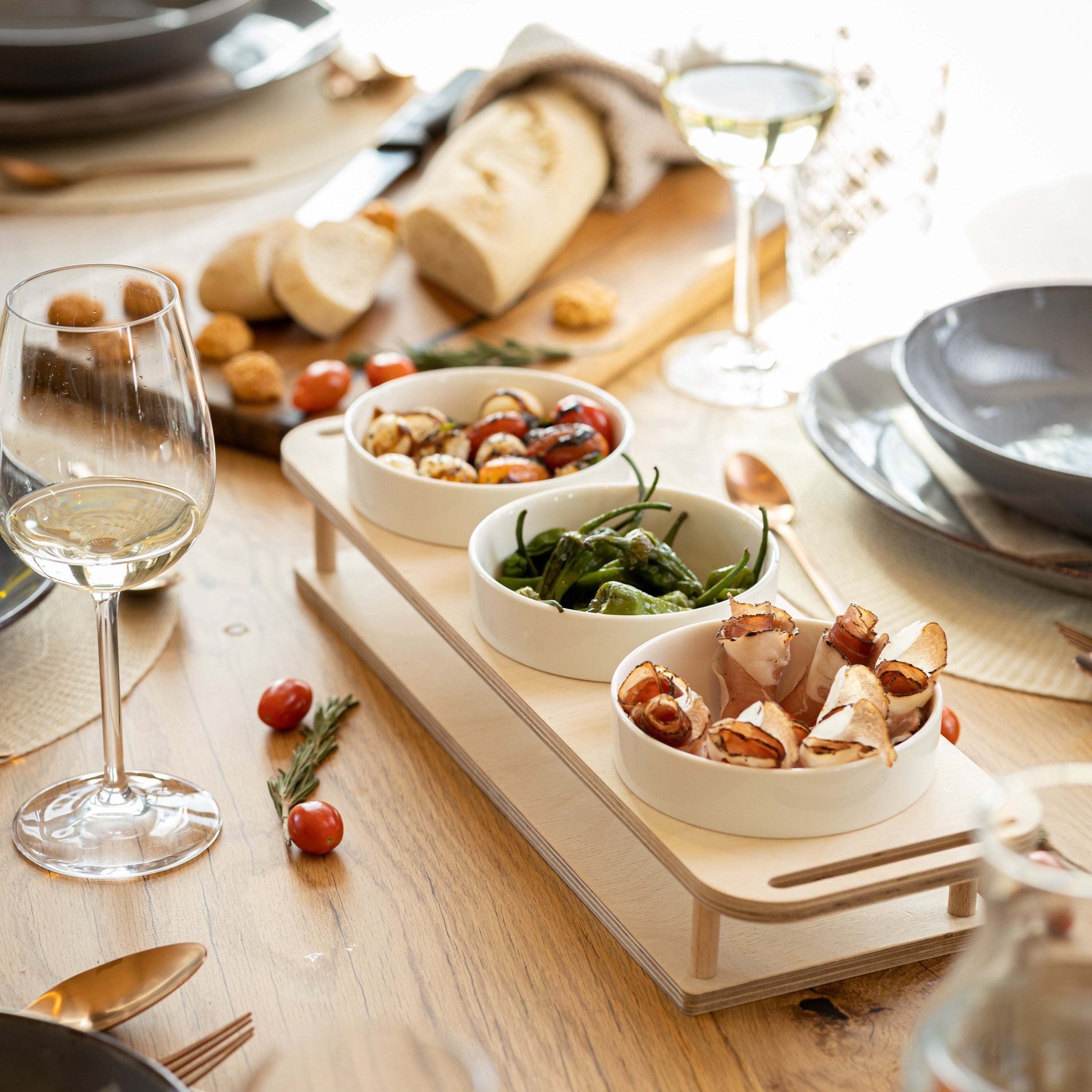 HOTTY TapasBar with ceramic bowls in a wooden tray, surrounded by tapas on a dining table.