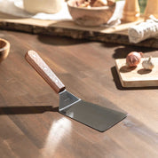 Pfannenwender mit Holzgriff und Edelstahlfläche auf Holztisch.
