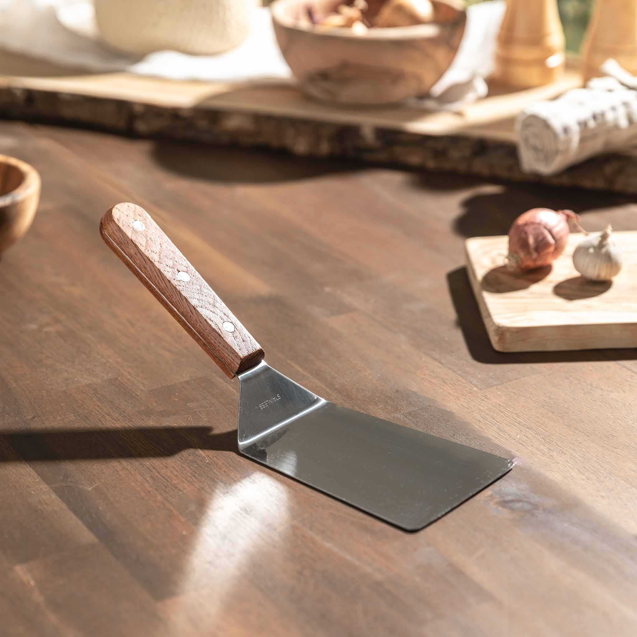 Pfannenwender mit Holzgriff und Edelstahlfläche auf Holztisch.