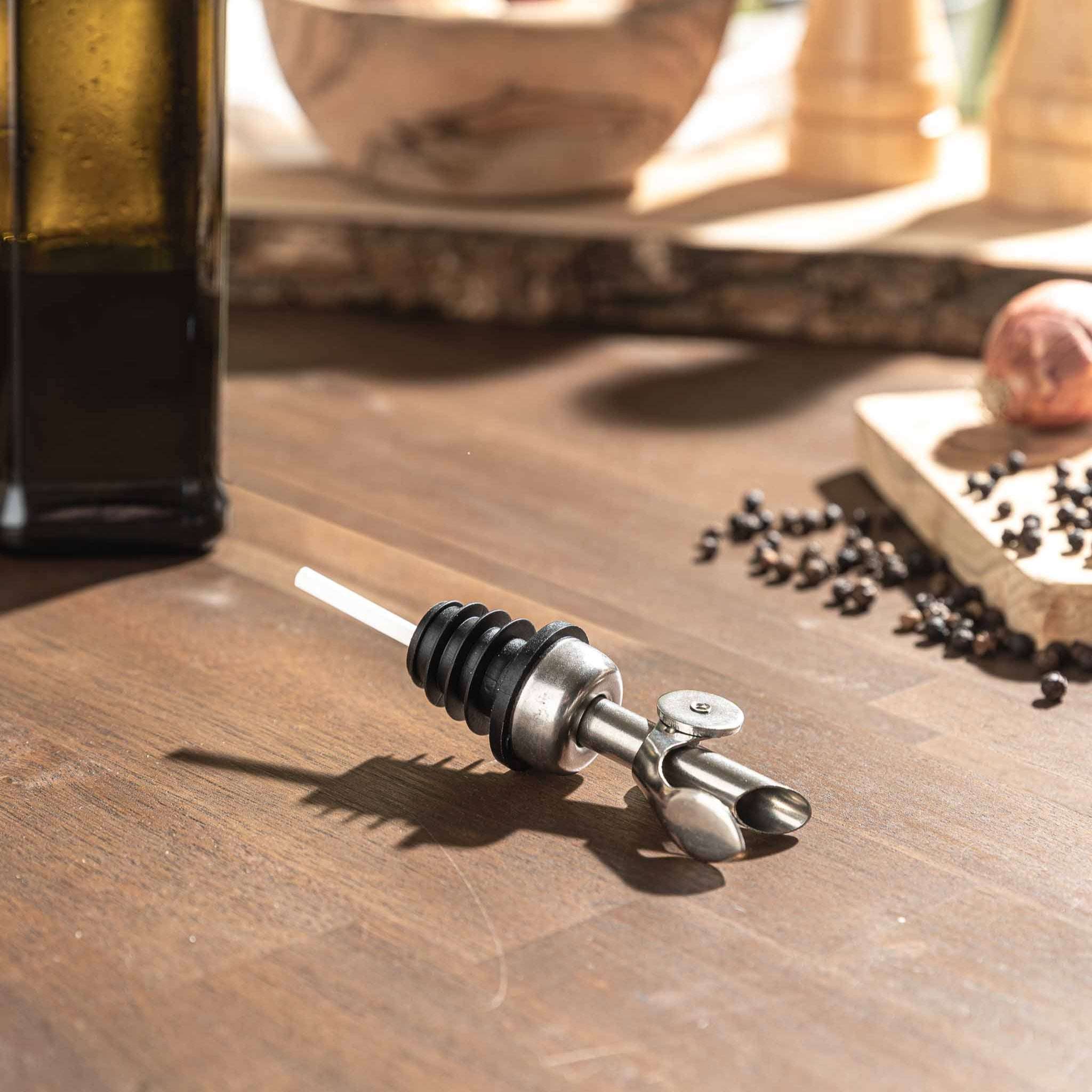 Ausgießer on wooden table with bottle, featuring sleek stainless steel design for precise pouring.