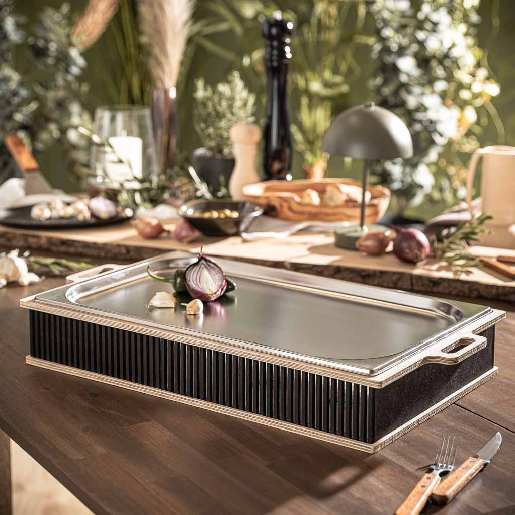 Hotty Legacy Wärmplatte auf elegant gedecktem Tisch, ideal zum Warmhalten von Grillgut, umgeben von Grillzubehör und Gewürzen.